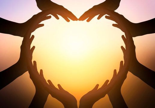Silhouetted hands forming the shape of a heart against a bright sunlit background.