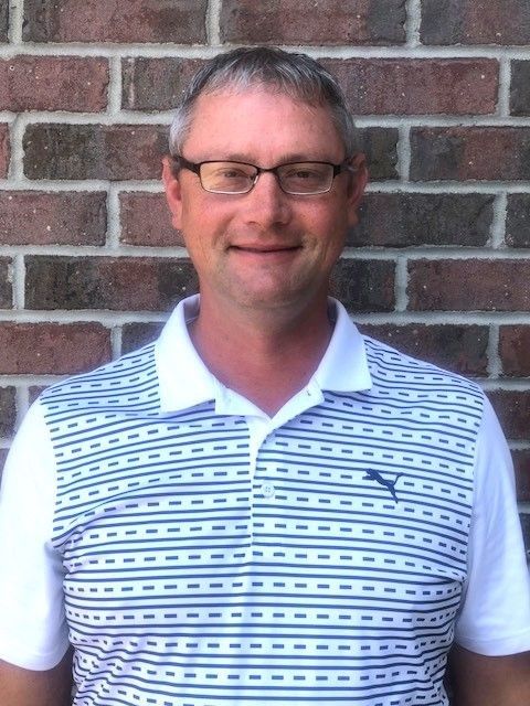 Person wearing glasses and a striped polo shirt standing in front of a brick wall.