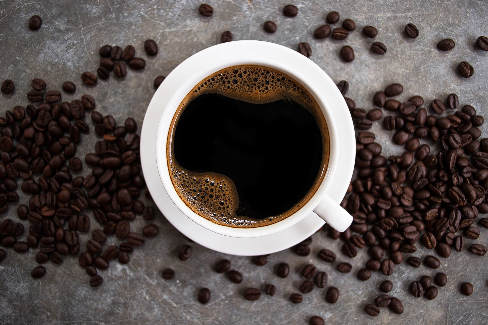 Black coffee in a white glass placed on an old cement table with coffee beans.