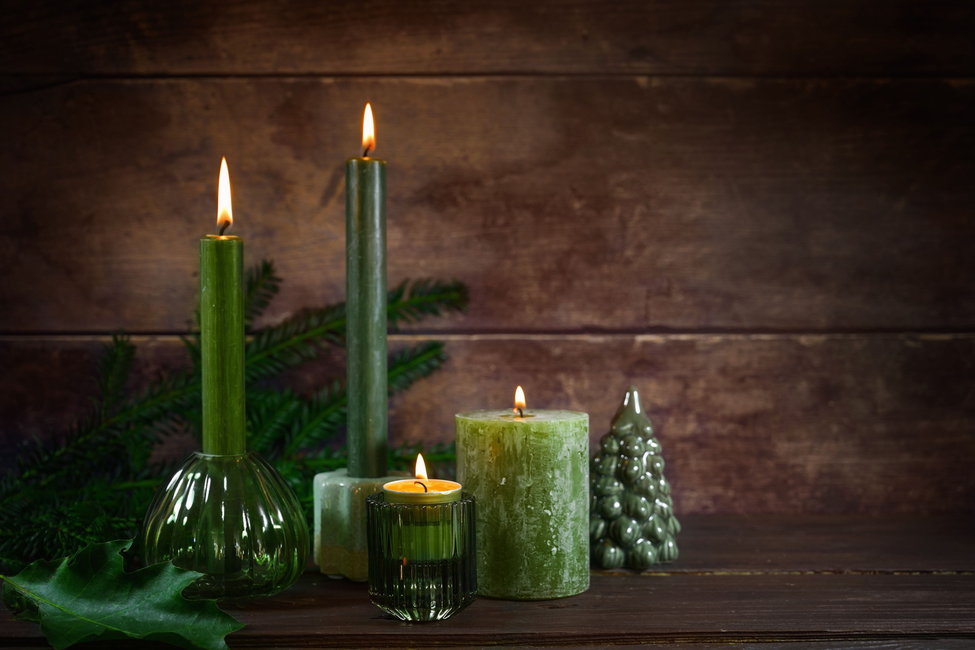 Four different green candles, evergreen twigs and simple Christmas decoration, dark rustic wooden background, natural decor for advent, New Year and seasonal holidays, copy space