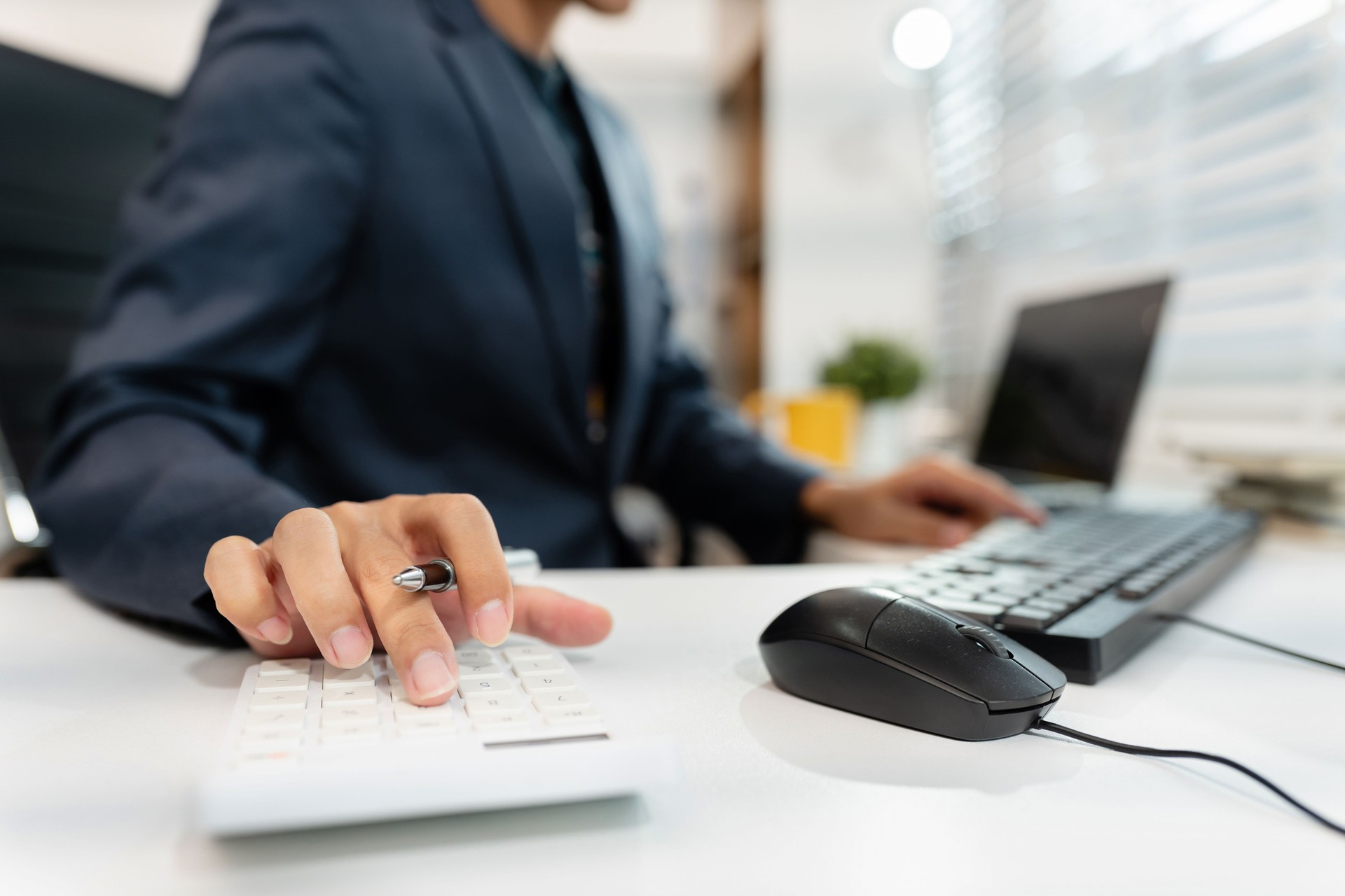 Male businessman working on desk office with using a calculator to calculate the numbers and business report talk smart phone on office desk, finance accounting concept.