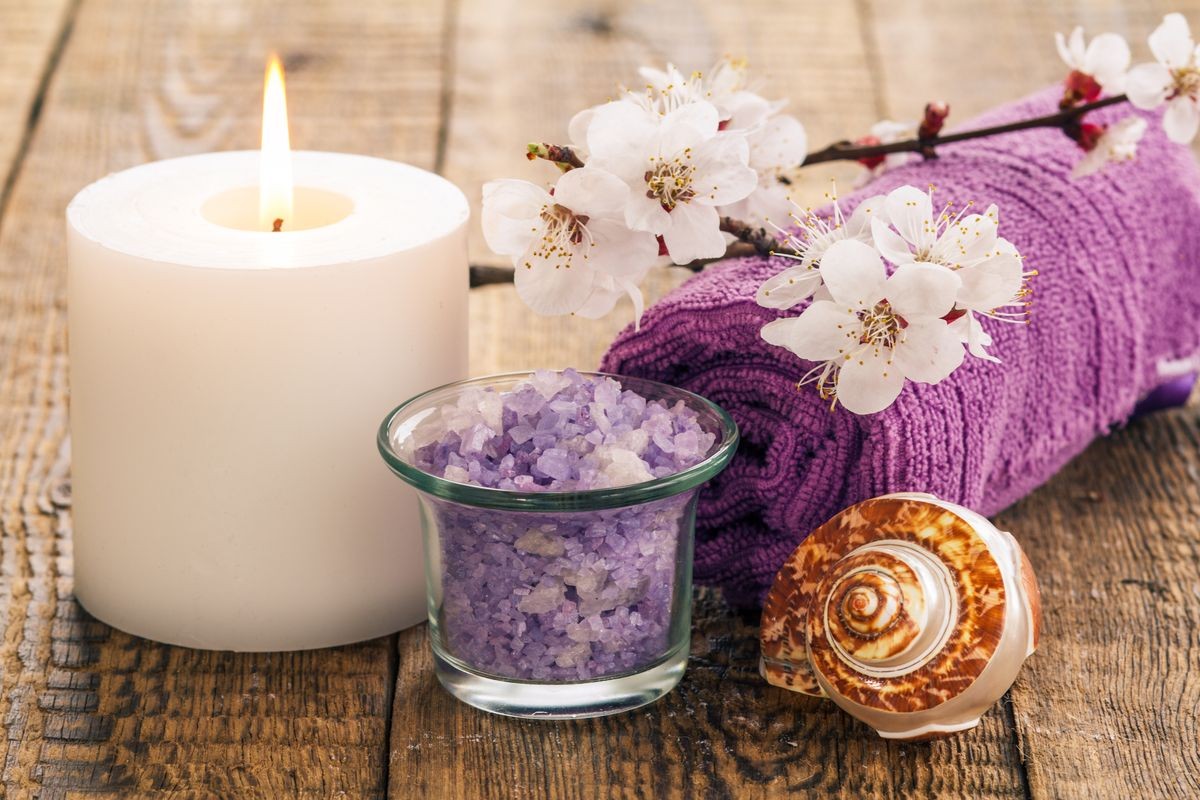Sea salt in glass bowl with towel for bathroom procedures, sea shell and  burning candle with flowering branch of apricot tree on the background. Spa products and accessories