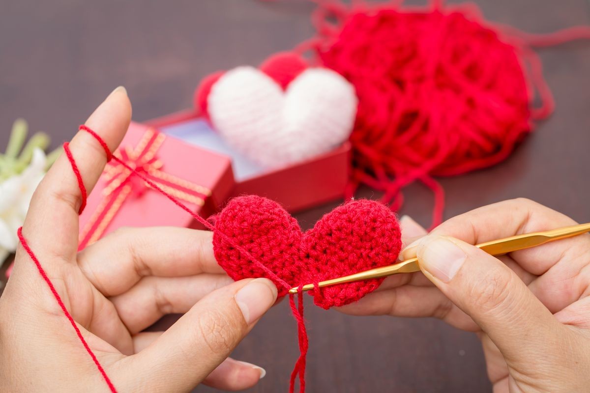 The woman is knitting red heart-shaped with yarn as art crafts to give someone love in the public park, for give supporting when people get who lack of desire with love and Valentine day concept.